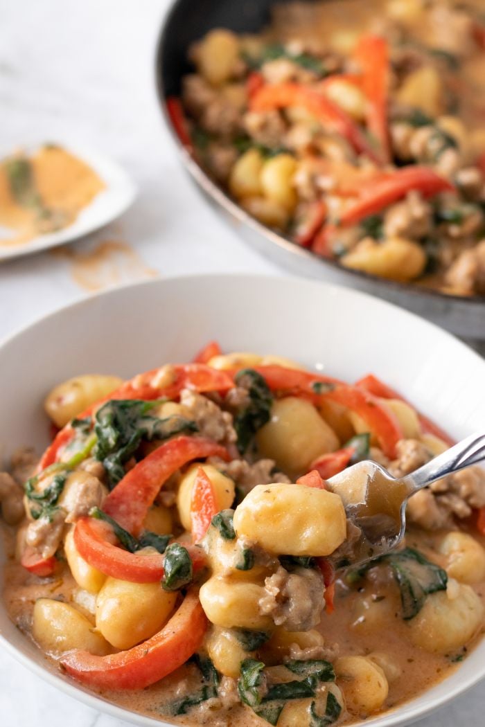 a large bowl of creamy gnocchi and sausage with the pan in the background
